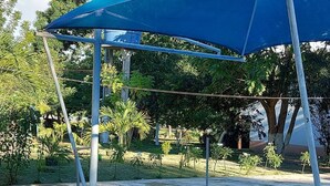 A swimming pool with a blue shade structure, surrounded by greenery and trees.