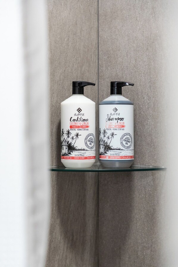 Two bottles of Alaffia Coconut & Ginger Conditioner on a glass shelf. - New Build Modern Condo in the heart of Traverse City (Traverse City)