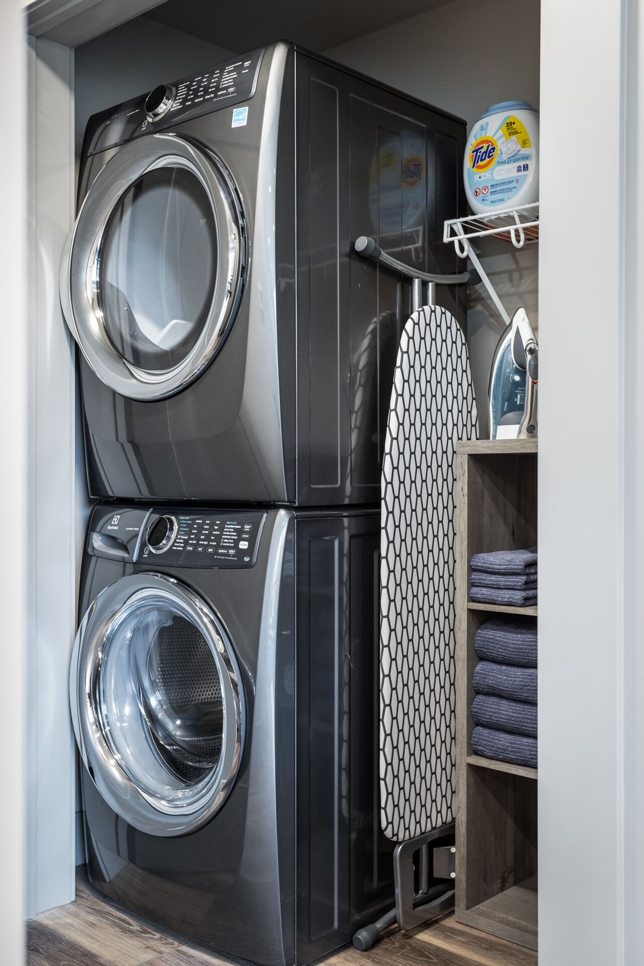 A compact laundry room with two stacked front-loading washing machines and a drying rack.