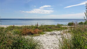 Una spiaggia con sabbia e scarsa vegetazione, che si affaccia su un mare calmo sotto un cielo sereno.