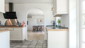 Una cucina moderna con isola centrale, zona pranzo con tavolo e sedie, e vista su una sala da pranzo attraverso un arco.