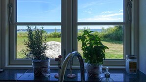 Cucina con un'ampia finestra vista su una zona erbosa e il mare. Due piante in vaso sul davanzale.