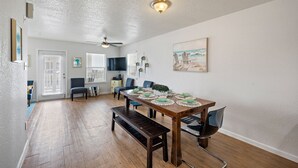 Un coin repas avec une table en bois dressée pour quatre personnes, un banc et un ventilateur de plafond.