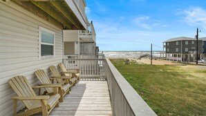 Une terrasse en bois avec des fauteuils Adirondack, un balcon et une vue sur l’océan.