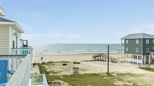Une propriété située en bord de mer, dotée d’une terrasse en bois, d’un petit escalier menant à la plage et offrant une vue sur l’océan.