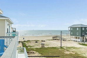 A beachfront property with a wooden deck, a small staircase leading to a beach, and a view of the ocean.