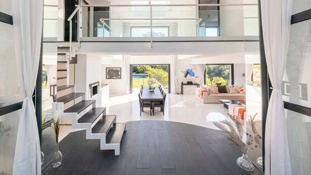 A modern interior with a staircase leading to a second floor, a dining area, and a living space with a sofa and coffee table.
