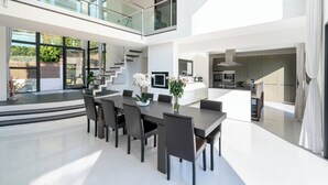 Um espaço de estar moderno e aberto, com área de jantar, cozinha e escadaria de vidro que conecta dois andares.