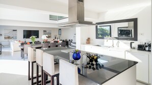 A modern kitchen with a central island, a dining area with chairs, and a large window.