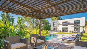 A covered outdoor area with wicker furniture, a pool, and a modern building in the background.