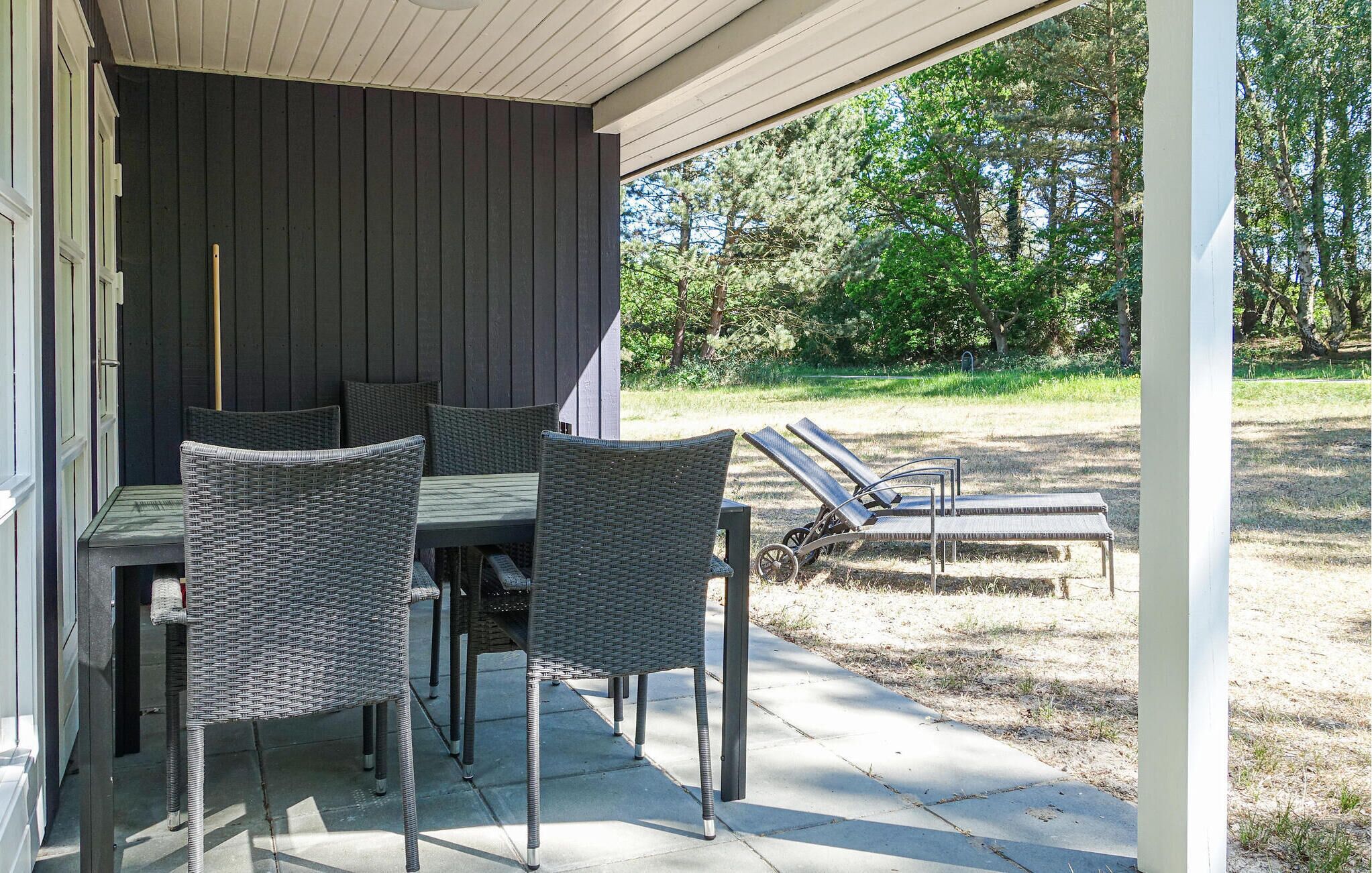Eine Terrasse im Freien mit Korbmöbeln, einem Tisch und zwei Liegestühlen.