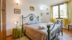 Una cama bien hecha con cabecera, una mesita de noche con lámpara y una ventana con cortinas.