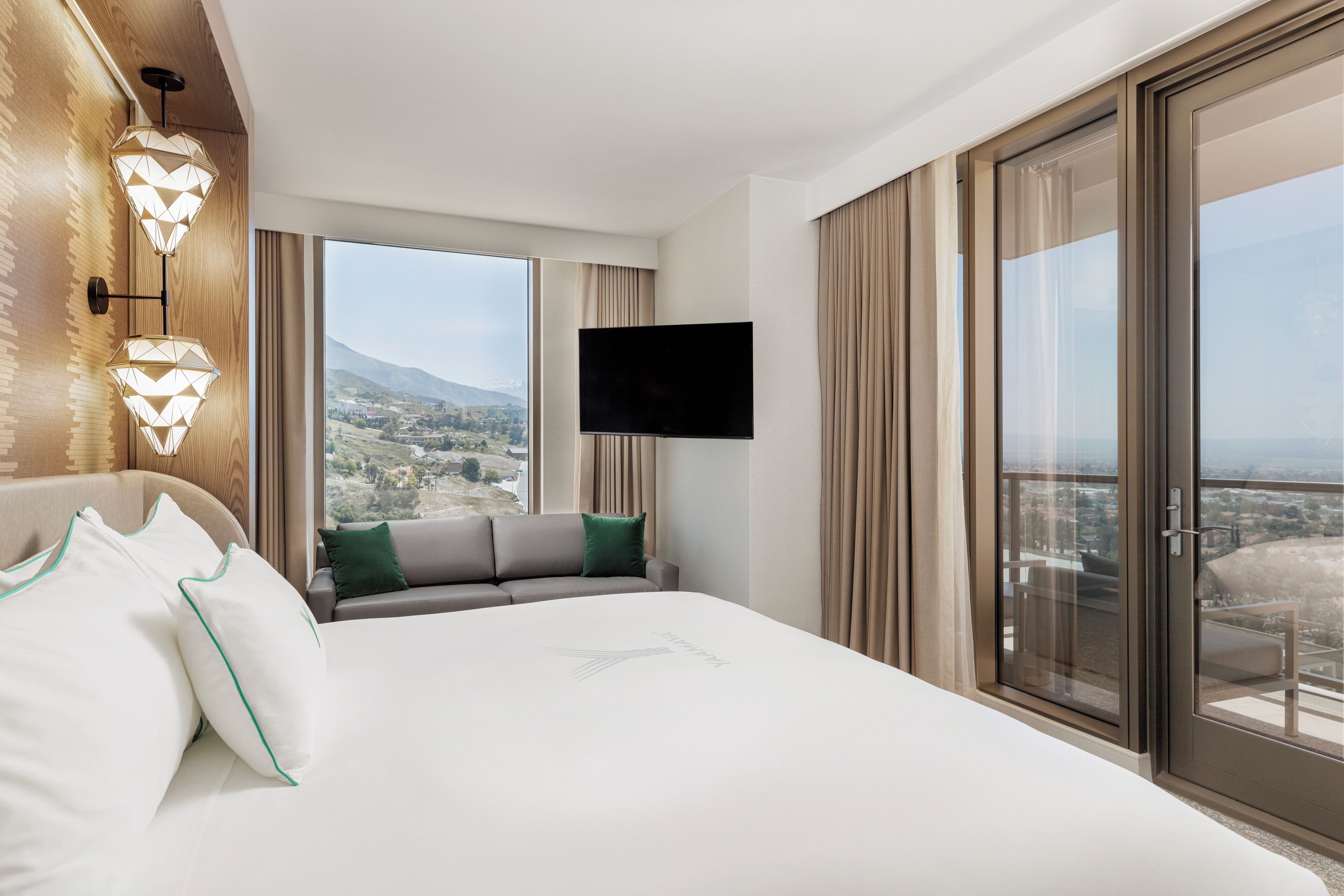 Habitación de hotel con una cama grande, un sofá, un televisor y un balcón con vista a la ciudad.