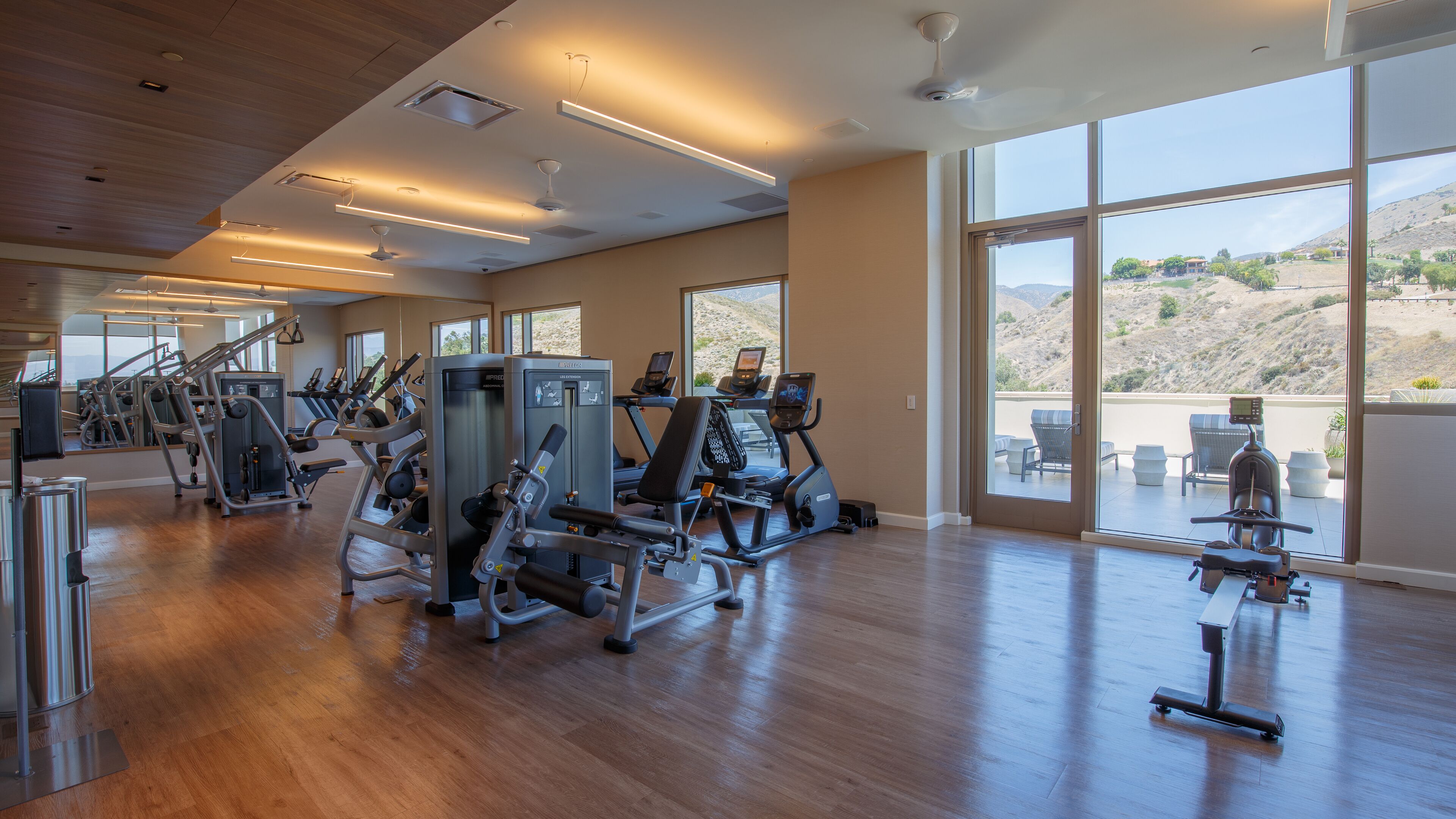 Un gimnasio moderno con diversos equipos de ejercicio, amplias ventanas que ofrecen vistas a un paisaje montañoso.