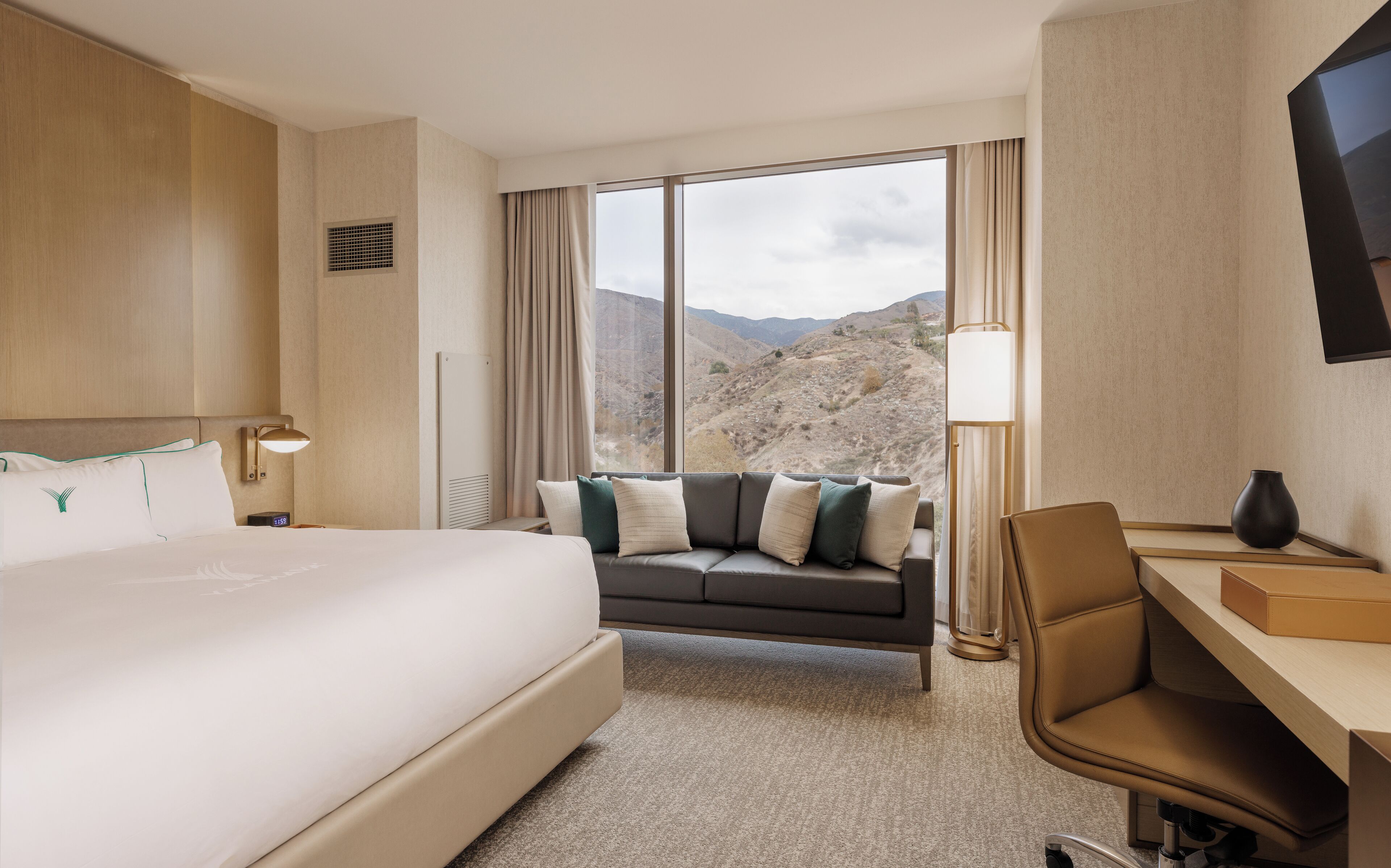 A hotel room with a large bed, a sofa, a desk, and a view of mountains.
