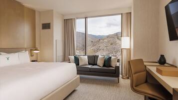 A hotel room with a large bed, a sofa, a desk, and a view of mountains.