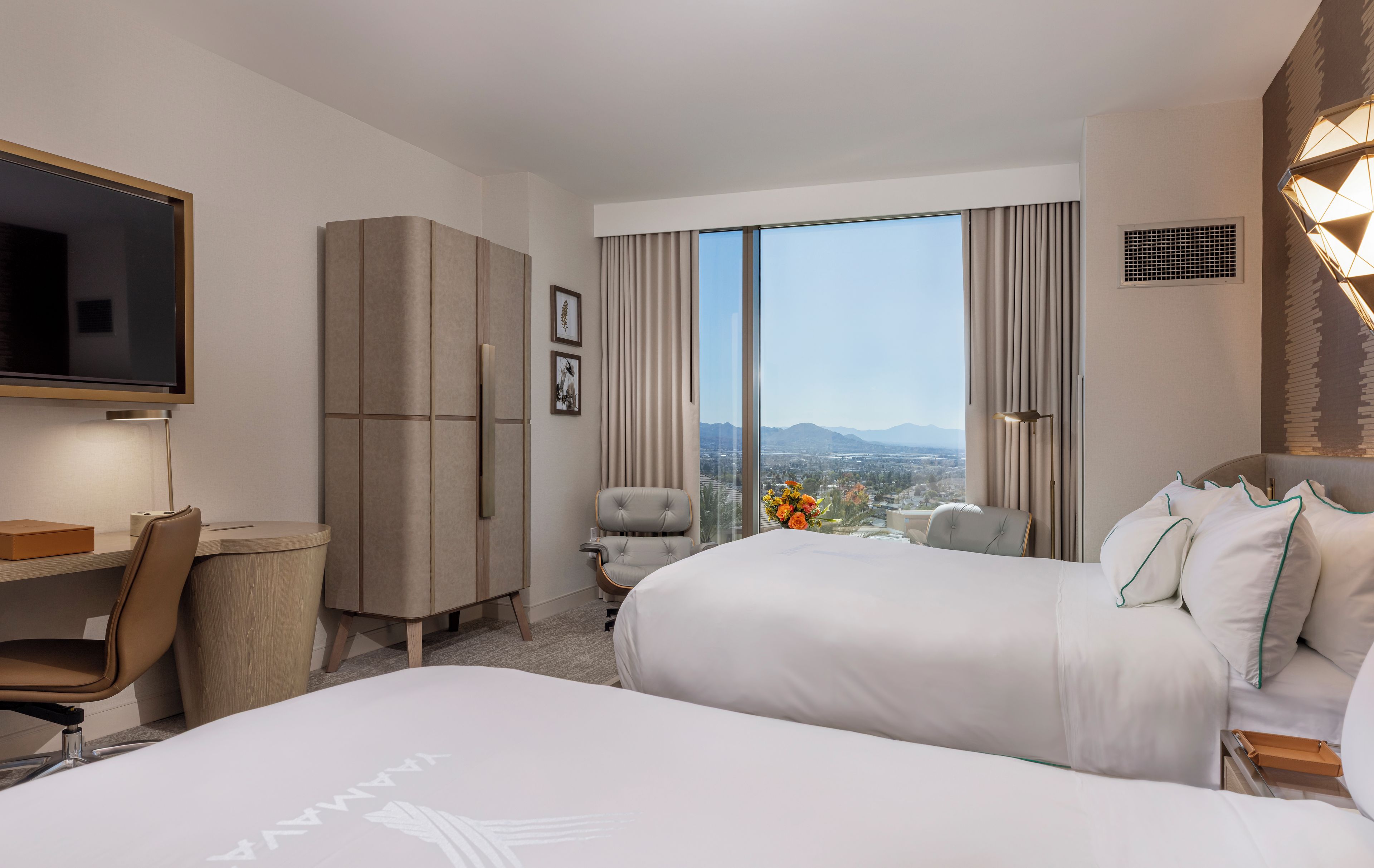 A hotel room with a large bed, a desk, a chair, a television, and a view of the city.