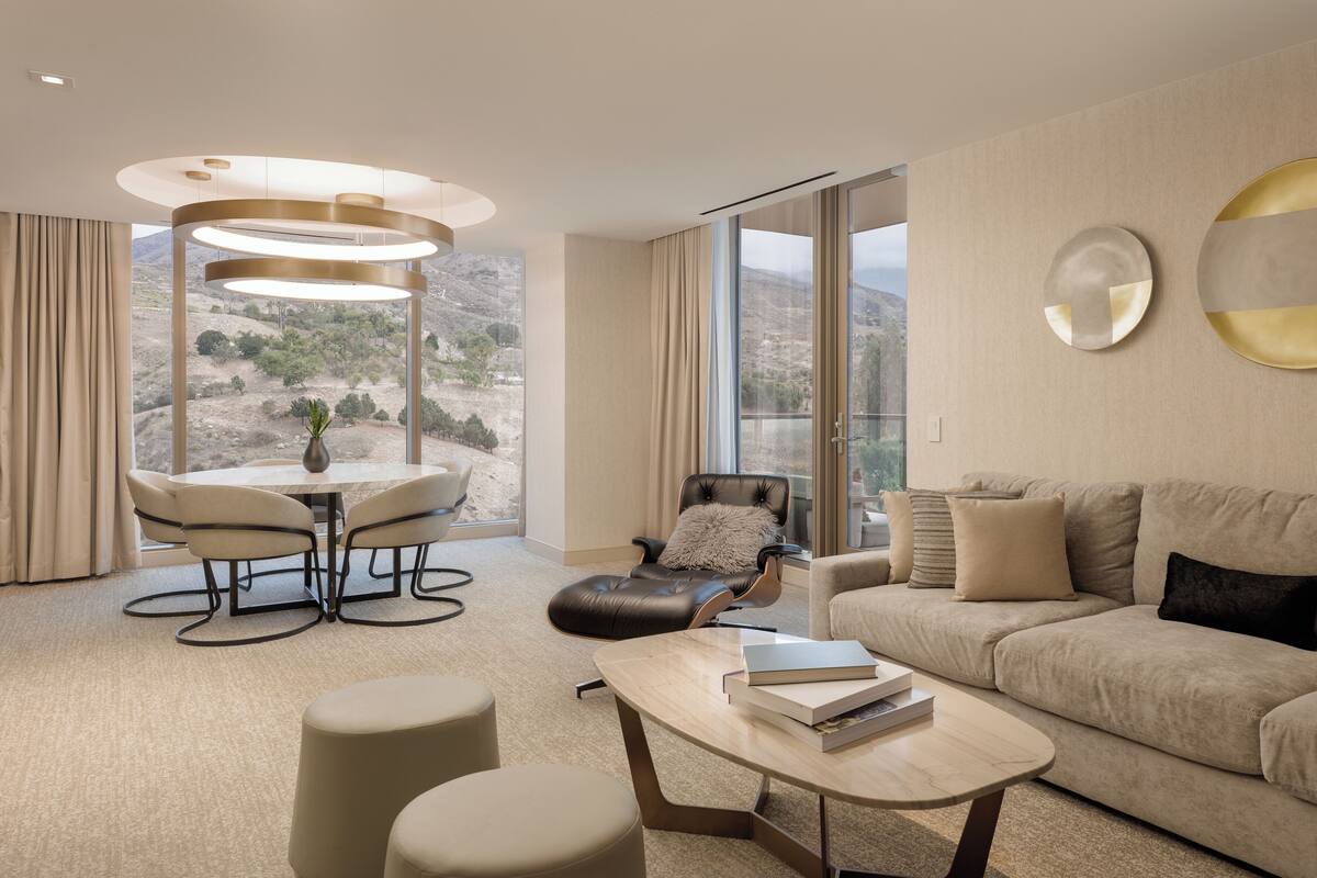 A modern living room with a round table, a sofa, and a large window offering a view of a mountainous landscape.