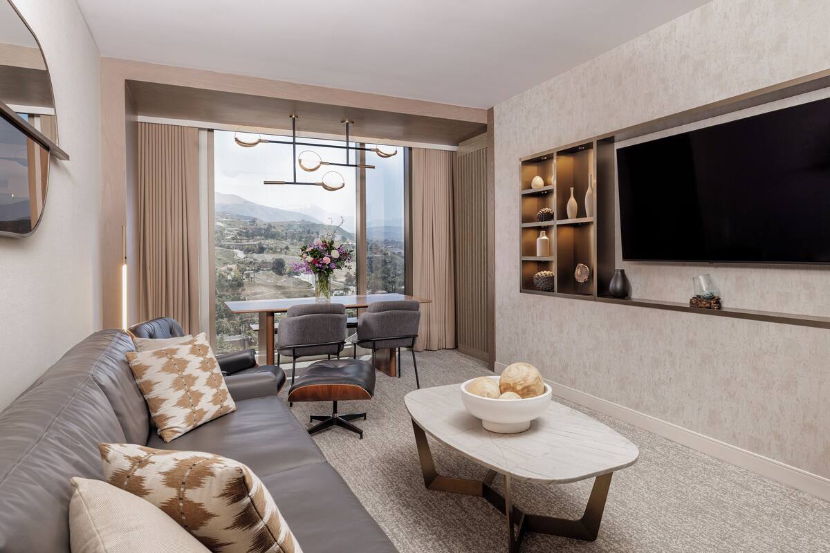 A modern living room with a sofa, a dining table, and a TV mounted on the wall.
