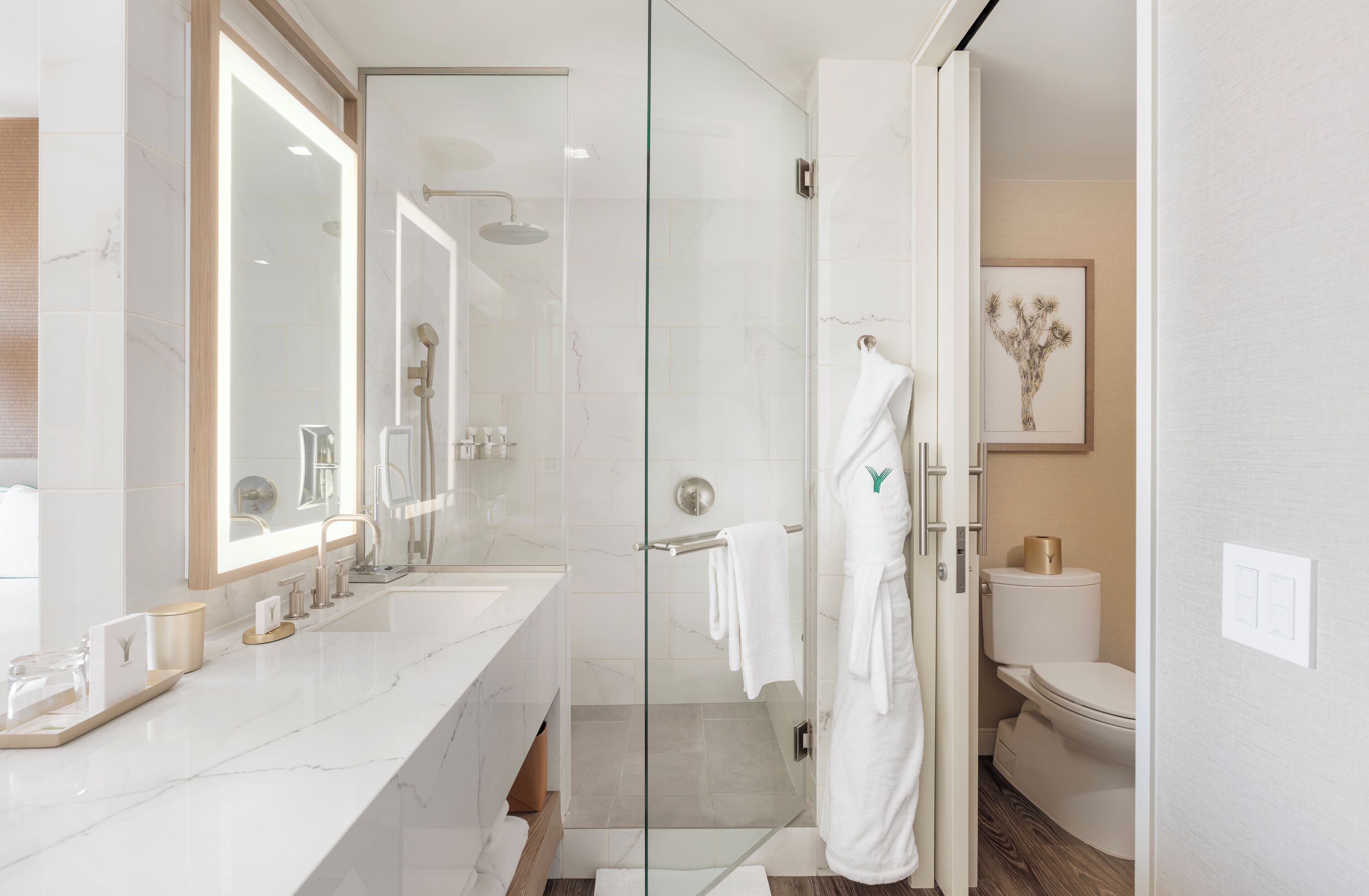 A modern bathroom with a glass-enclosed shower, a large mirror, and a white sink with toiletries.