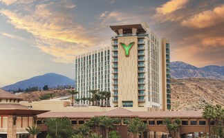 Un hotel moderno con un llamativo logo verde, varios pisos y un paisaje montañoso al fondo.