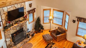 Amplia sala de estar con chimenea de piedra, techo de madera y ventanas grandes.