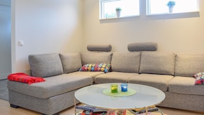 A modern living room with a grey sectional sofa, a round glass coffee table, and two windows with potted plants. - Amazing home in Köpingsvik with WiFi (Köpingsvik)