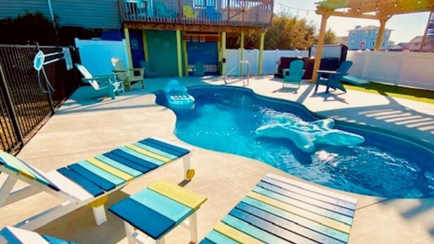A backyard with a swimming pool, lounge chairs, and a pergola. - Short Steps to Beach! Private Pool! Hot Tub! Linens Included! Family Favorite. (Kitty Hawk)