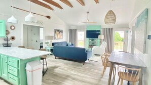 A spacious living area with a large sofa, a dining table, and a kitchen area with a green island. - Short Steps to Beach! Private Pool! Hot Tub! Linens Included! Family Favorite. (Kitty Hawk)