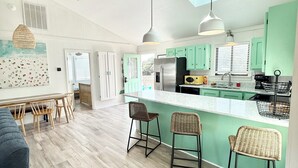 A spacious kitchen with wooden beams, a central island with bar stools, and a dining area with a long table and chairs. - Short Steps to Beach! Private Pool! Hot Tub! Linens Included! Family Favorite. (Kitty Hawk)