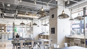 Un interior de restaurante moderno con una larga mesa de comedor, múltiples sillas, iluminación colgante y vistas a la ciudad a través de amplios ventanales.