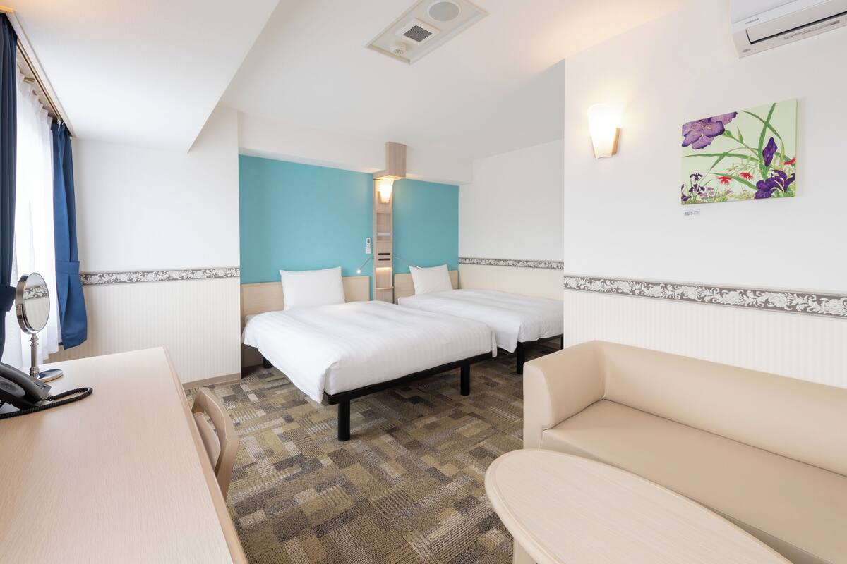 Une chambre d’hôtel avec deux lits, un bureau avec un téléphone, un canapé et un climatiseur fixé au mur.