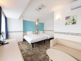 Habitación de hotel con dos camas, un escritorio con teléfono, un sofá y aire acondicionado instalado en la pared.