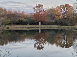 Un étang paisible, avec une croix au centre, entouré d’arbres aux couleurs automnales.
