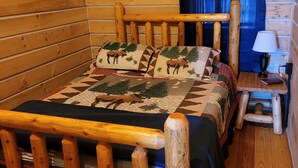 Puisesta hirrestä rakennettu mökki, jossa on sänky, pieni pöytä ja lamppu.