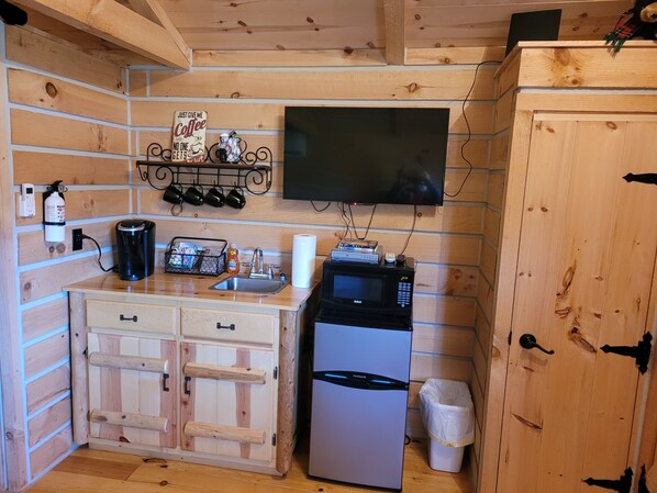 Une cuisine compacte aux murs en bois, dotée d’un four à micro-ondes encastré, d’une machine à café, d ’un évier et d’un petit réfrigérateur.