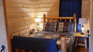 A log cabin bedroom with a wooden bed, two bedside lamps, a blue curtain, and a wooden headboard.