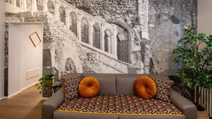 A room with a grey sofa, a patterned throw, and a large mural of an ancient structure.