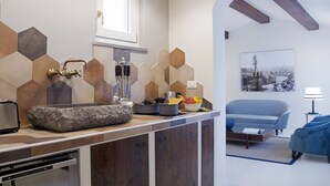 Eine moderne Küche mit Spüle aus Stein, einem Fenster über der Spüle und einer Rückwand mit sechseckigen Fliesen. Es gibt einen Essbereich mit einem blauen Sofa und einer Lampe.