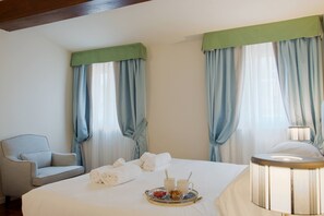 A hotel room with a bed, a chair, a tray with breakfast items, and a lamp.