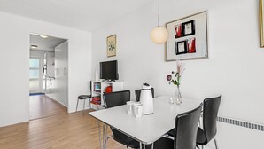 Un espace repas moderne avec une table blanche, des chaises noires, un vase blanc orné de fleurs et un tableau accroché au mur.