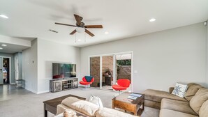 A modern living room with a sofa, coffee table, and red chairs. There is a TV and a ceiling fan. - Modern East Hill Home, Premier Location! (Pensacola)