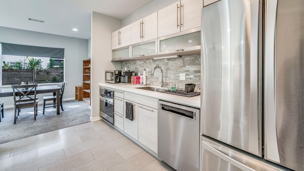 A modern kitchen with stainless steel appliances, light-colored cabinetry, and a large window providing natural light. - Modern East Hill Home, Premier Location! (Pensacola)