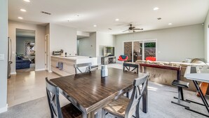 A spacious living area with a dark wooden dining table, modern kitchen, and a cozy seating area with a red chair and a keyboard. - Modern East Hill Home, Premier Location! (Pensacola)