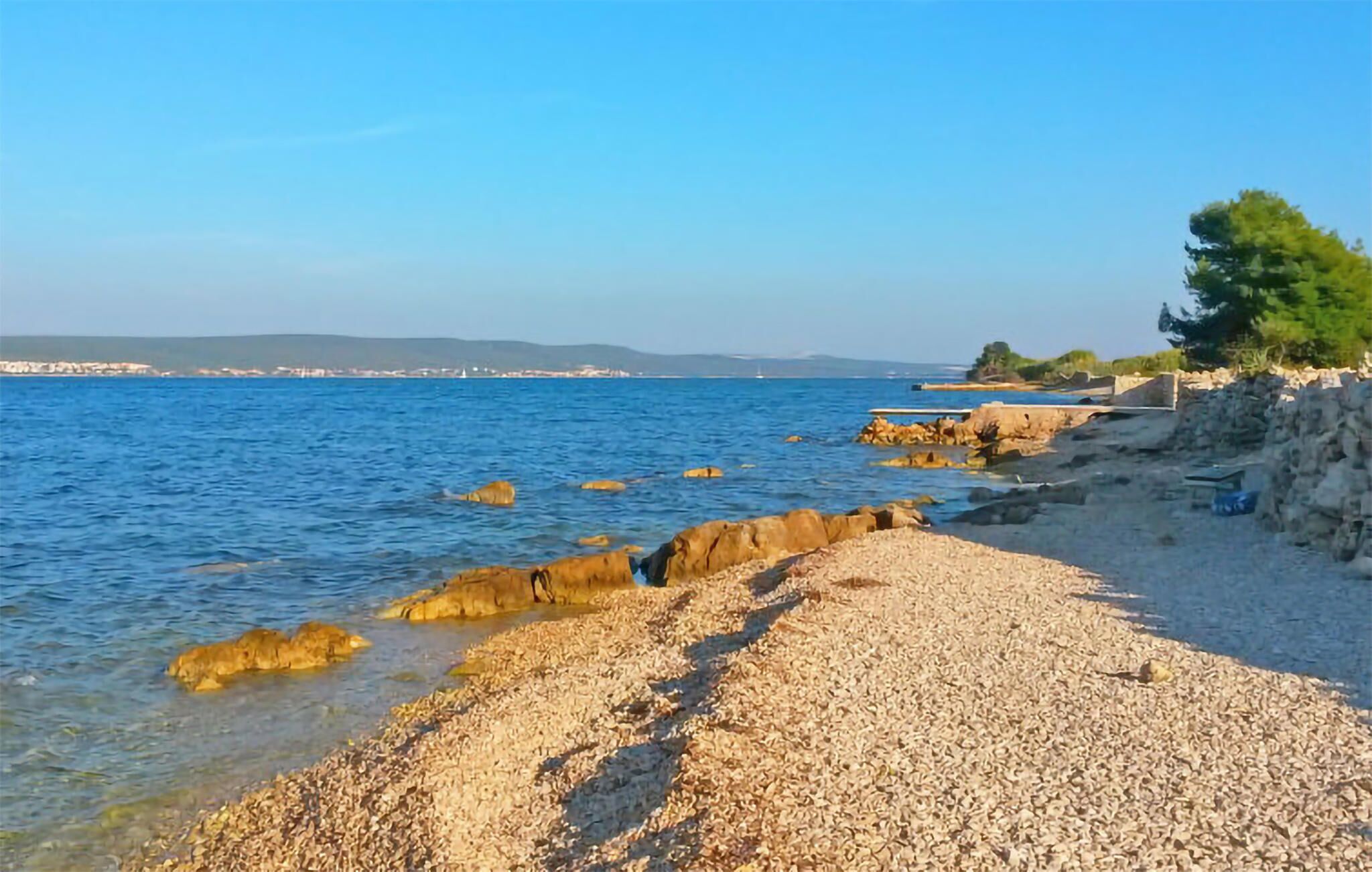 Een kiezelstrand met helderblauw water en rotsachtige uitstulpingen.