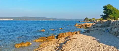Een kiezelstrand met helderblauw water en rotsachtige uitstulpingen.