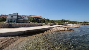 Una propietat costanera amb vista clara al mar, una paret de pedra i un camí pavimentat que condueix a un edifici amb balcons.