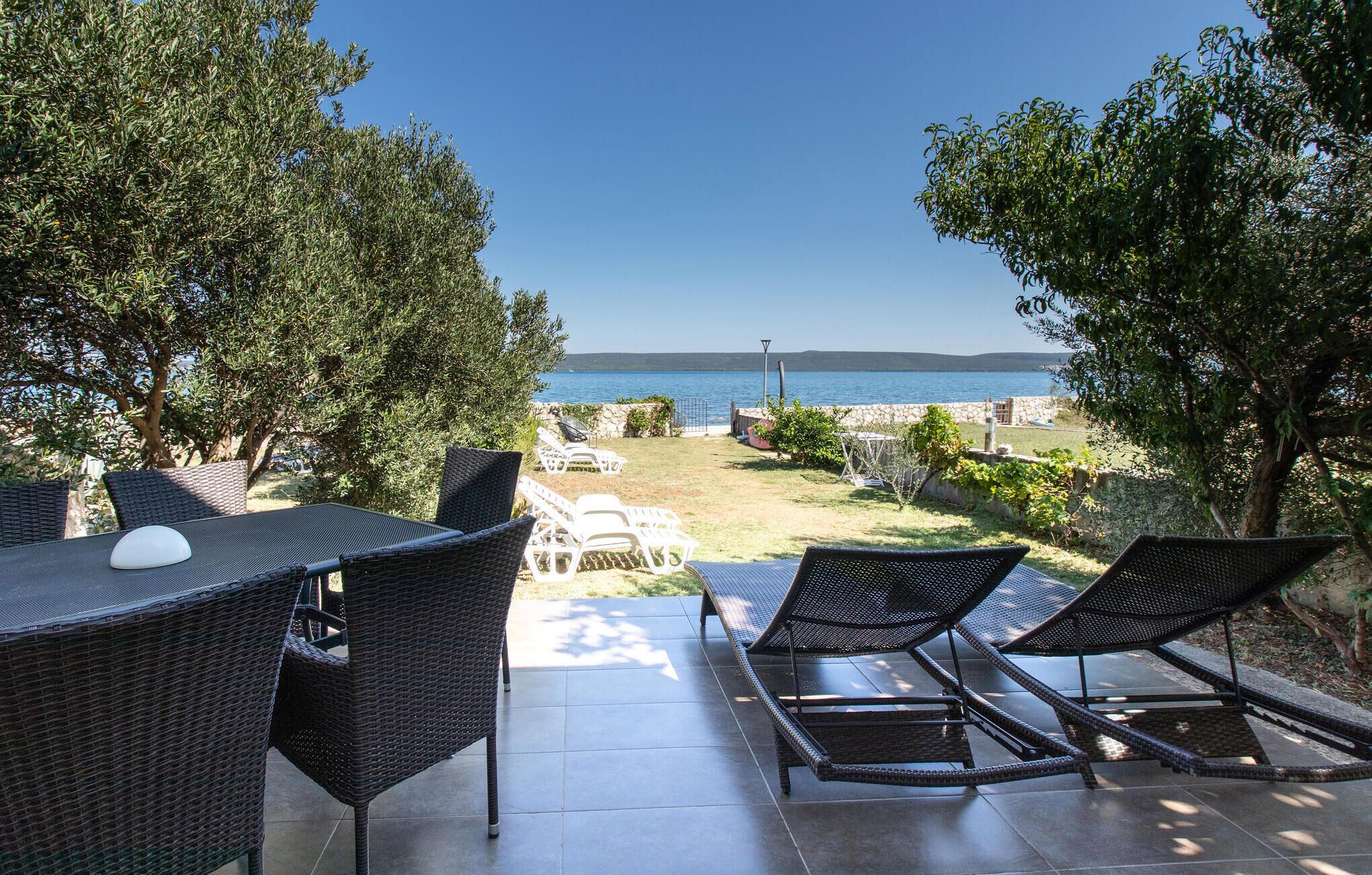 An outdoor patio with wicker furniture, a table, and a view of the sea.