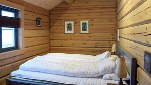 Una habitación acogedora tipo cabaña de madera, con una cama, un ventanal y dos cuadros en la pared.