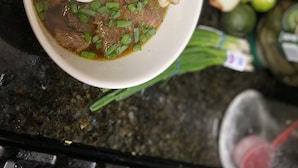 Eine Schüssel Suppe mit Fleisch, Eiern und Frühlingszwiebeln auf einer Küchenarbeitsplatte.